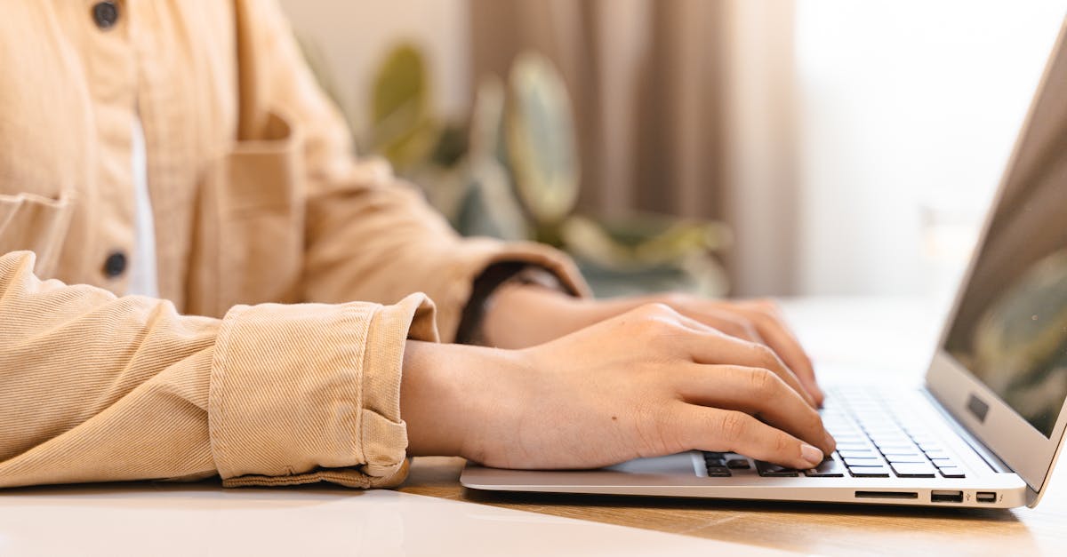 Close-up of hands typing on a laptop indoors, wearing a casual jacket.